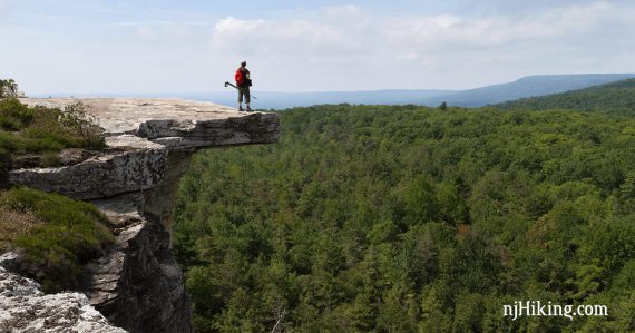 Hiker standing on a rocky ledge jutting off of a cliff.