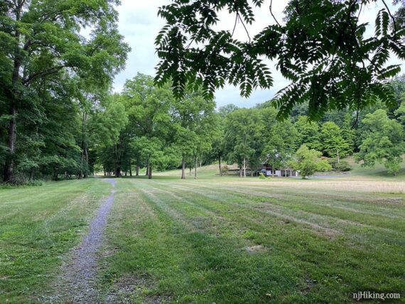 Narrow dirt trail through an open grassy area with a house off on the side.