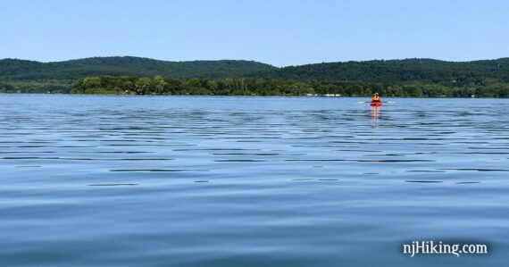 Kayaker on a flat blue lake with rolling green hills in the distance.