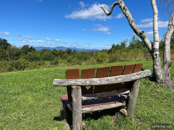 Rustic bench on a hill with a view of the Catskill Mountains in the distance.