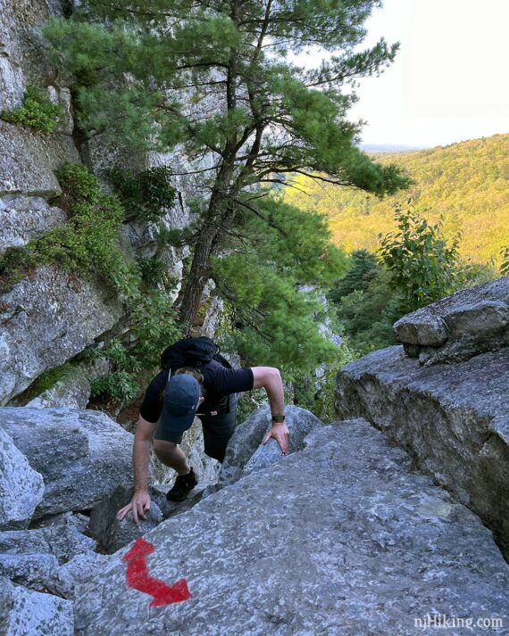 Hiker at the top of a scramble with a curved red arrow painted on rock.